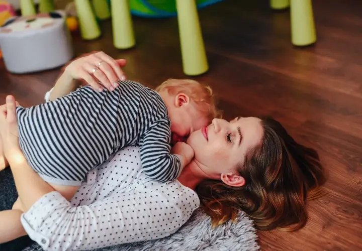Mama i dziecko leżą na podłodze. Dziecko przytula się do mamy. To piękny przykład, co to stymulacja rozwoju poprzez bliskość i zabawę.