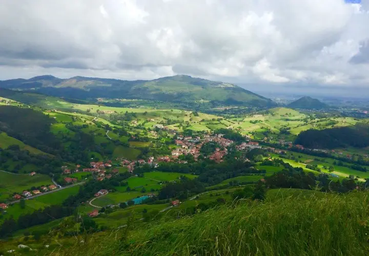 Paisaje verde y montañoso, con un pueblo en el valle. La **ruta Tetas de Liérganes** ofrece vistas espectaculares.