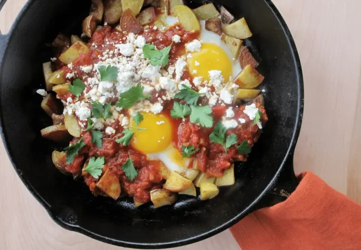 Plat savoureux : recette pomme de terre oeuf avec sauce tomate, fromage émietté et persil frais, servi dans une poêle en fonte.