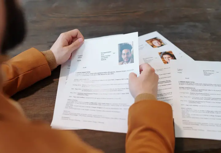 Osoba przegląda dokumenty CV z portretami.