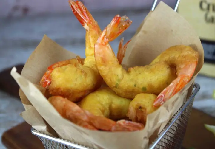 Crujientes gambas a la gabardina doradas, servidas en una cesta metálica con papel marrón.