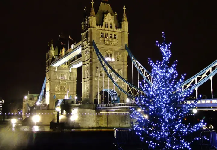 Albero di Natale illuminato con luci blu davanti al Tower Bridge di Londra, evocando l'atmosfera dei mercatini di Natale in inglese.