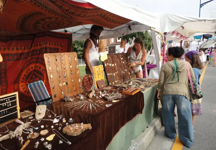 En el **mercado hippie Argaños**, se exhiben collares y pulseras artesanales. Una vendedora muestra su mercancía a dos clientas.