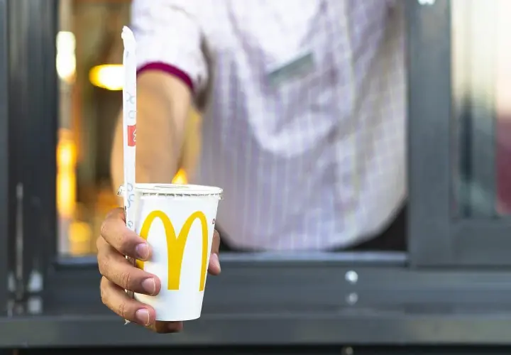 Ręka podaje kubek z McDonald's. Zastanawiasz się, ile kalorii ma cola zero z McDonald's? Ten napój ma zero kalorii.