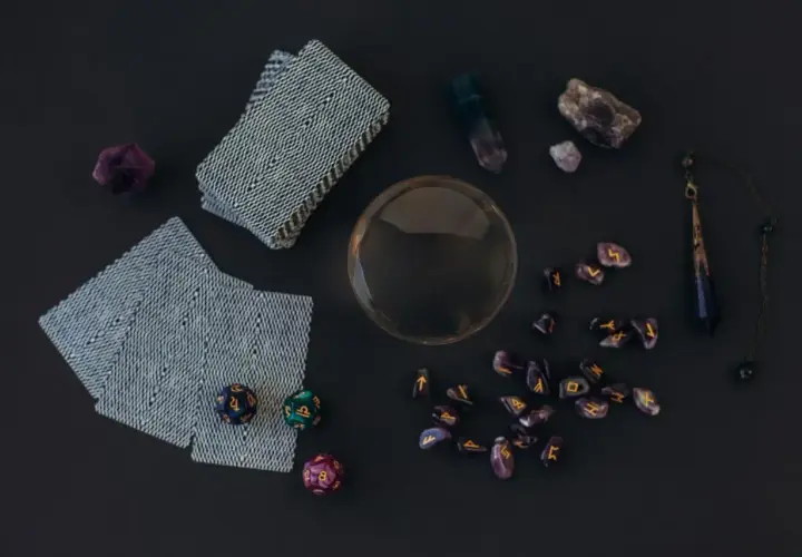 Na stole leżą karty tarota, kryształy, runy i kula. Może to zapowiedź przyszłości, jak 10 denarów tarot.