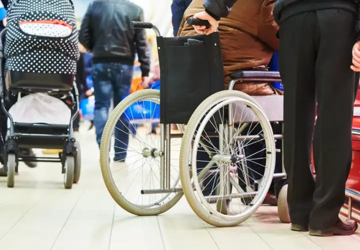 Opiekunowie osób niepełnosprawnych, wspierani przez 500 plus, poruszają się po sklepie. Wózek inwalidzki i spacerowy obok.