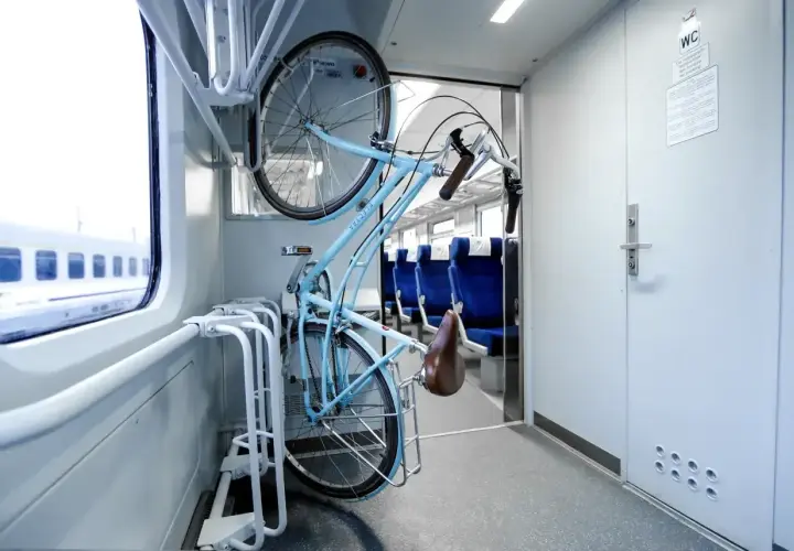 Błękitny rower zawieszony w specjalnym uchwycie w wagonie Pendolino. Obok siedzenia, za oknem pędzi krajobraz.