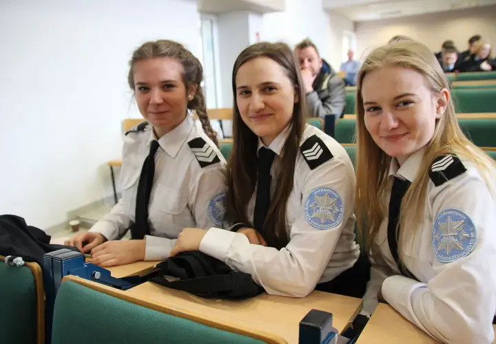 Trzy uśmiechnięte studentki w mundurach policyjnych siedzą w sali wykładowej. To przyszłość policji, ich studia policyjne dopiero się zaczynają.