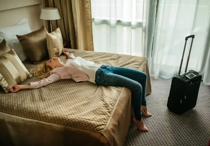 Zmęczona podróżą kobieta odpoczywa na łóżku w hotelu. Szukasz noclegów w Polsce? Sprawdź oferty!