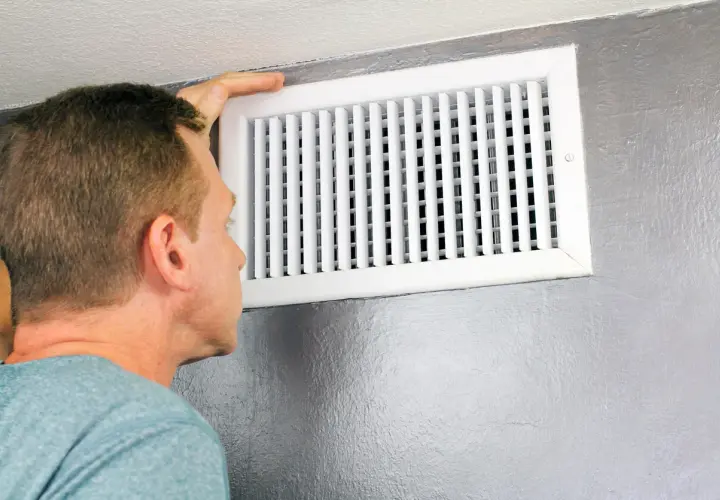 Hombre revisa un conducto de ventilación, mostrando diferentes tipos de rejillas para el aire acondicionado.