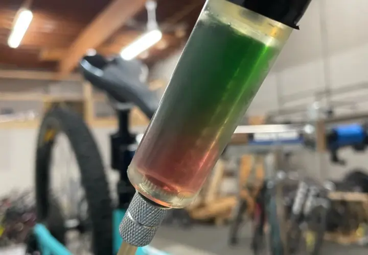 A syringe filled with red and green synthetic brake fluid, indicating a potential compatibility issue during a bike maintenance task.
