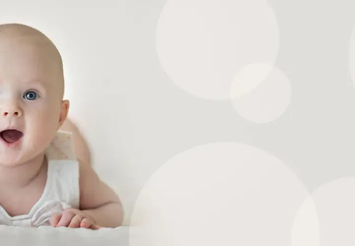 Uśmiechnięte, 4 miesięczne dziecko z niebieskimi oczami leży na brzuchu, patrząc z zaciekawieniem.