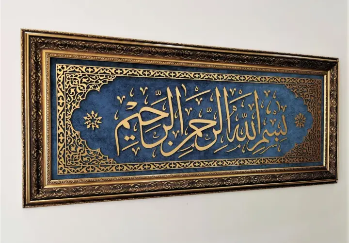 Złota kaligrafia "Bismillah" na granatowym tle, w bogatej, zdobionej ramie.