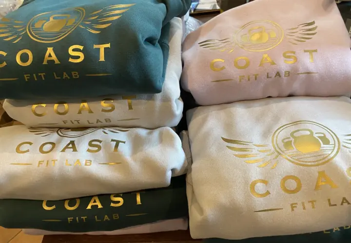 Stosik bluz klubowych w kolorach zielonym, różowym i kremowym, z złotym logo "COAST FIT LAB".