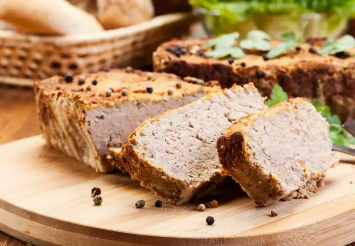 Pokrojony pasztet na desce, ozdobiony ziarnami pieprzu i natką pietruszki.