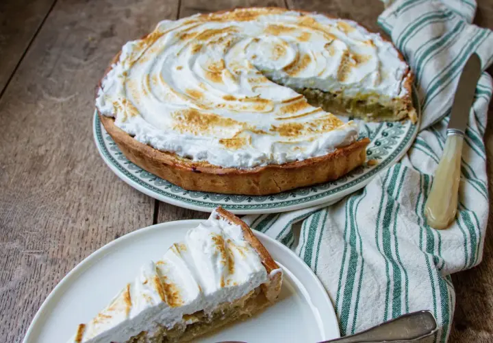 Tarte à la rhubarbe sur pâte feuilletée, recouverte d'une meringue dorée. Une part est servie sur une assiette.