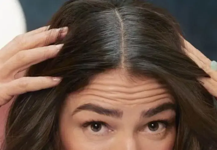 Mujer revisa su cabello oscuro con algunas canas. ¿Buscas como eliminar las canas para siempre?