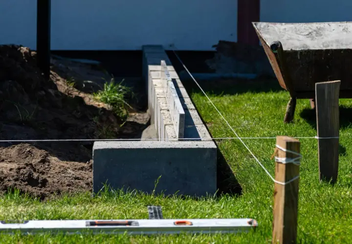 Budowa fundamentu pod ogrodzenie. Betonowe bloczki i poziomica wskazują precyzyjne wykonanie.