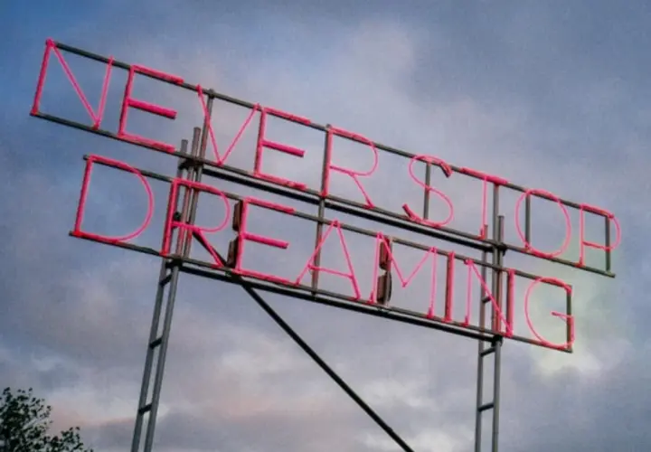 Insegna al neon rosa con la scritta "NEVER STOP DREAMING". Un promemoria ispiratore, come frasi sulla rinascita in inglese, per non smettere mai di sognare.