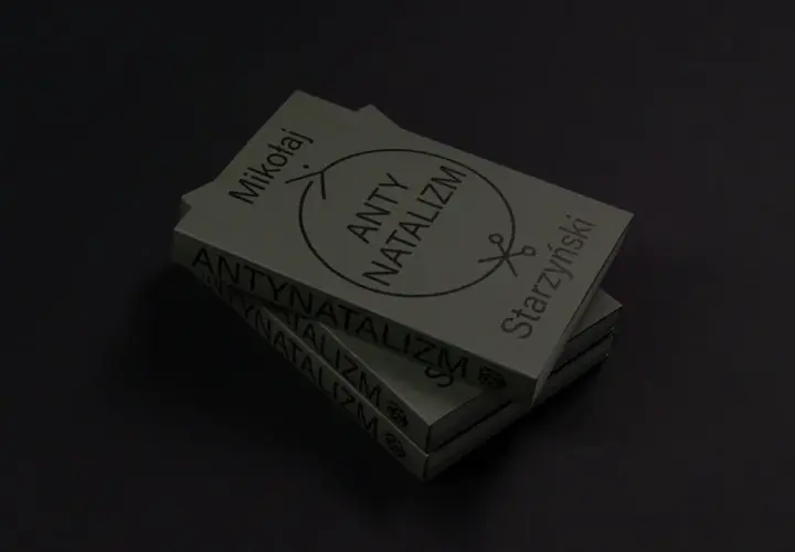 Stos książek z napisem "ANTY NATALIZM" i symbolem nożyczek. Dzieło Mikołaja Starzyńskiego.