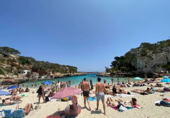 Słoneczna pogoda na Majorce, plaża pełna ludzi kąpiących się i opalających.