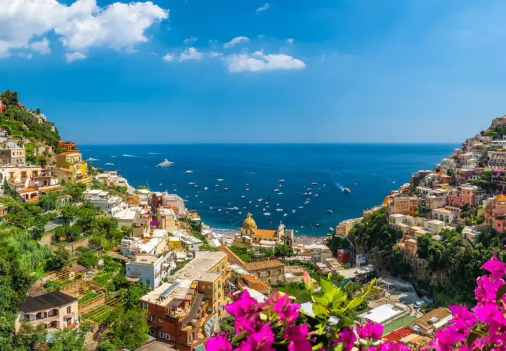 Colorful houses cascade down a cliffside to the sea, a picturesque view of the Amalfi Coast, a popular destination from Naples Airport.