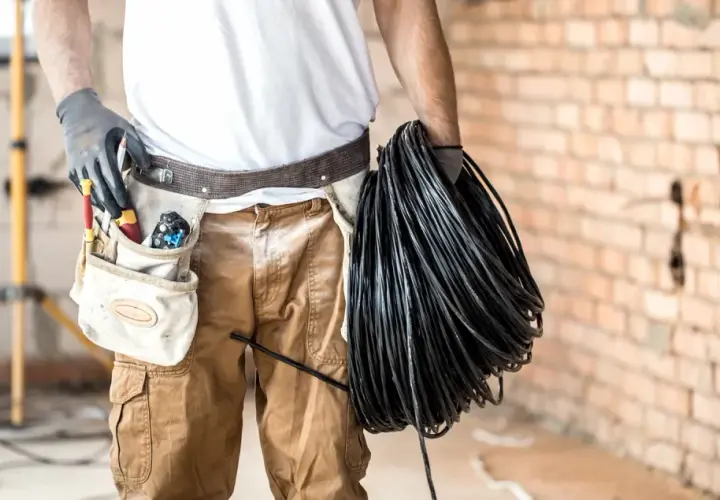 Elektryk z narzędziami w pasie trzyma zwój czarnego kabla. Czy będzie układany w peszlu, czy bezpośrednio w ziemi?