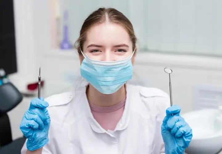 Uśmiechnięta asystentka stomatologiczna w maseczce i rękawiczkach trzyma narzędzia. Czas na egzamin!
