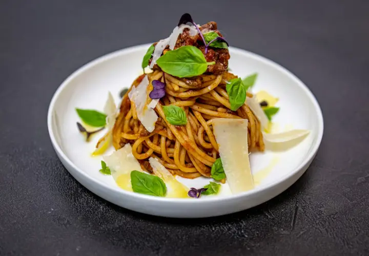 Pyszne spaghetti alla norma z sosem pomidorowym, bakłażanem, bazylią i parmezanem, podane na białym talerzu.
