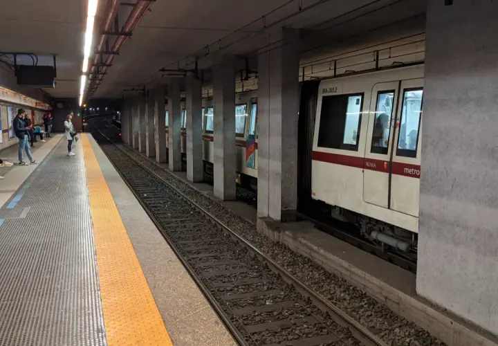 Persone attendono il treno alla stazione metro a Lepanto. Un convoglio bianco e rosso è fermo sui binari.