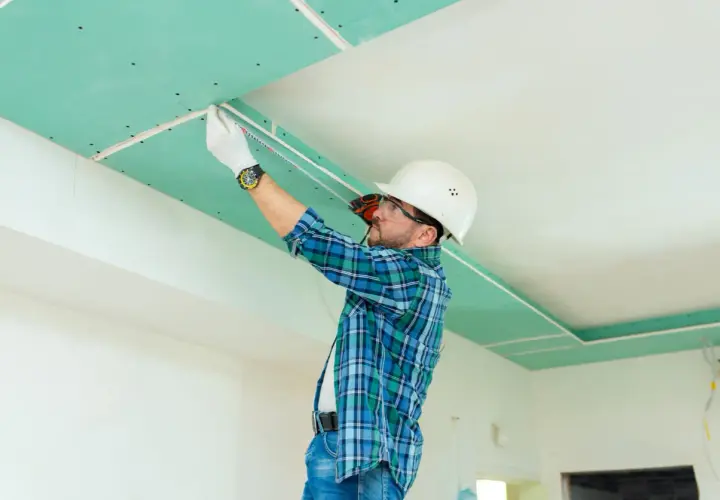 Operaio con casco misura il soffitto in cartongesso, pronto per lo stucco.