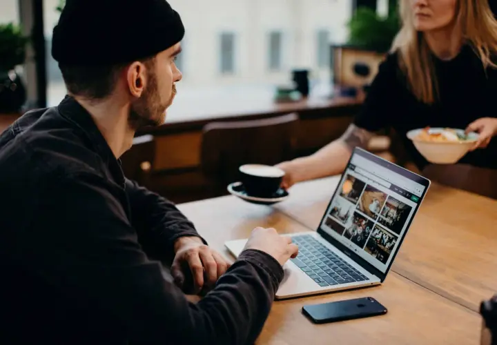 Mężczyzna w czapce pracuje na laptopie, analizując dane. Obok stoi filiżanka kawy. To praca ux researchera.