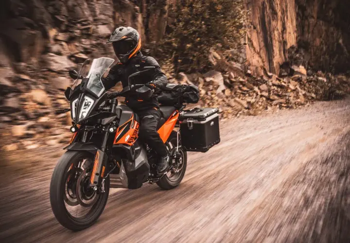 Motociclista en KTM naranja y negra, equipada para aventura, recorre un camino de tierra. La mejor moto trail media cilindrada lista para la exploración.