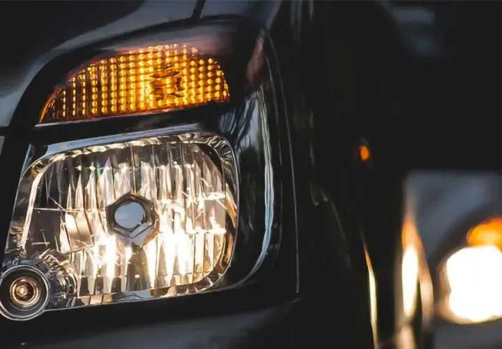 Luces cruce de un coche, con el intermitente naranja encendido y el faro principal iluminando. Otro coche se ve al fondo.