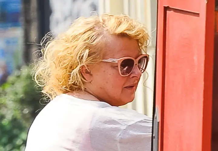 Magda Gessler bez peruki, w okularach przeciwsłonecznych, z kręconymi blond włosami, w białej koszulce.