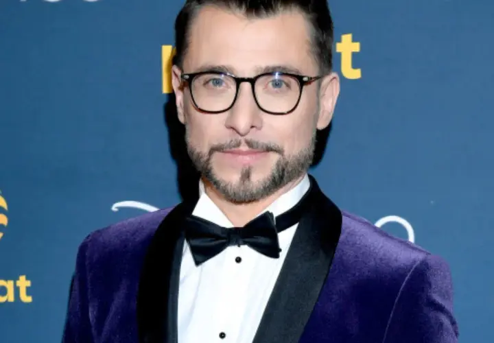 Kacper Kuszewski w fioletowym aksamitnym garniturze z czarną muszką. Wygląda elegancko, jakby wybierał się na galę z żoną.