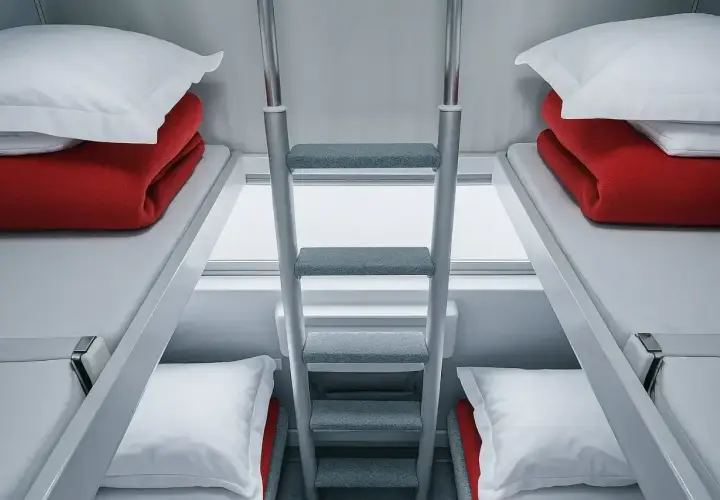 Wagon sypialny i kuszetka-różnice: dwa piętrowe łóżka z czerwonymi kocami i białymi poduszkami, połączone drabinką.