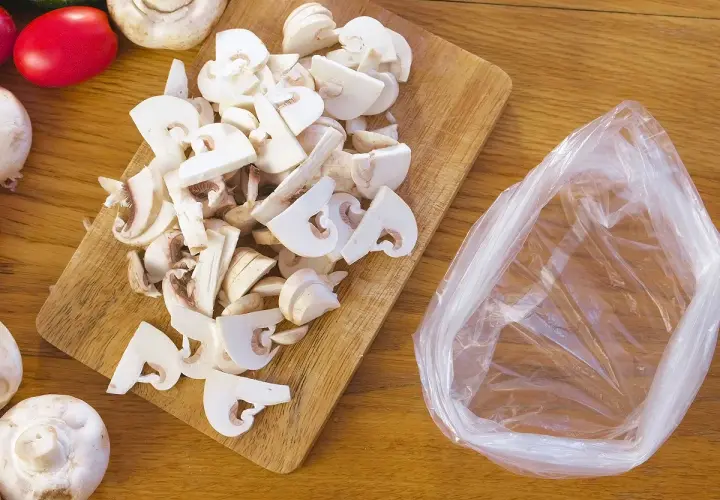 Champignons frais coupés sur une planche en bois, prêts à être mis dans un sac pour apprendre comment congeler des champignons frais.