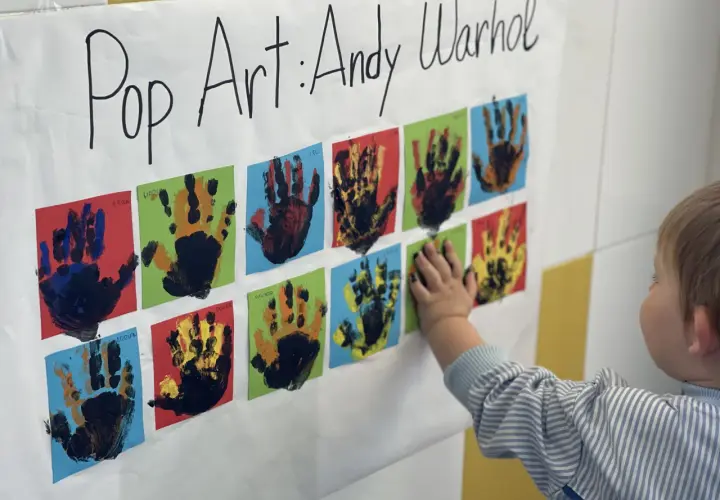 Manos pequeñas crean arte pop inspirado en Andy Warhol. Un niño toca una obra colorida, celebrando la creatividad infantil.