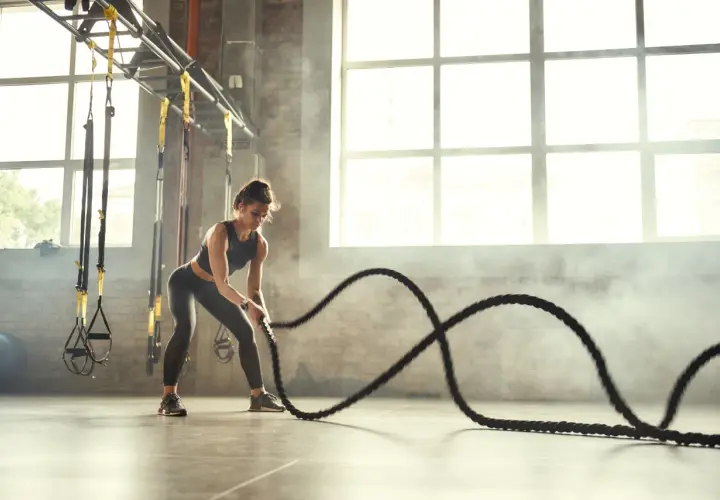 Kobieta ćwiczy z linami treningowymi, pokazując, crossfit co to za intensywny trening.