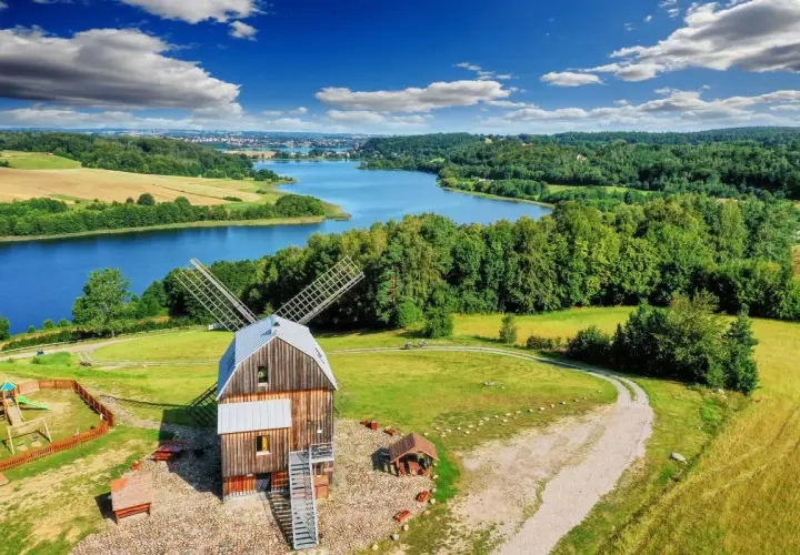 Drewniany wiatrak z tarasem widokowym na tle jeziora i lasów.