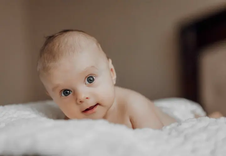 Niemowlę na brzuchu, z zaciekawieniem patrzące w obiektyw. Jego oczy, choć mogą sugerować zez u niemowlaka, są po prostu skupione na otoczeniu.