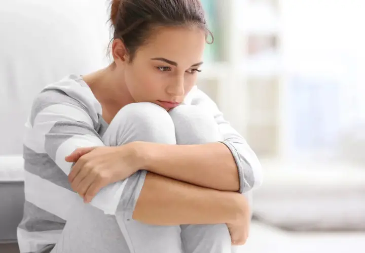 Ragazza con sguardo pensieroso, abbracciata alle ginocchia, simbolo di ansia ad alto funzionamento.