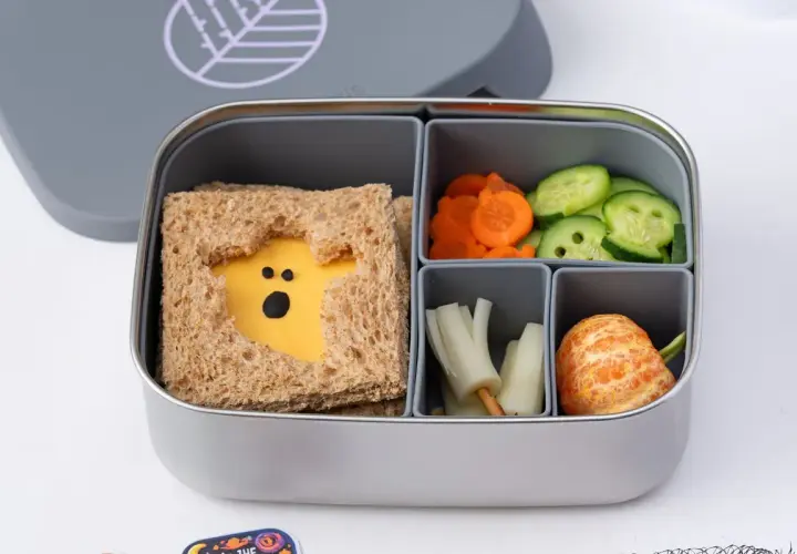 A spooky Halloween bento box with a ghost-shaped cheese sandwich, carrot slices, cucumber rounds, and a peeled tangerine.