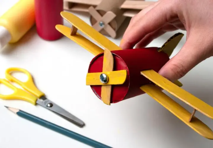 Un avión hecho con materiales de **avión manualidades**, sostenido por una mano. Tijeras y lápiz cerca, listos para crear más.