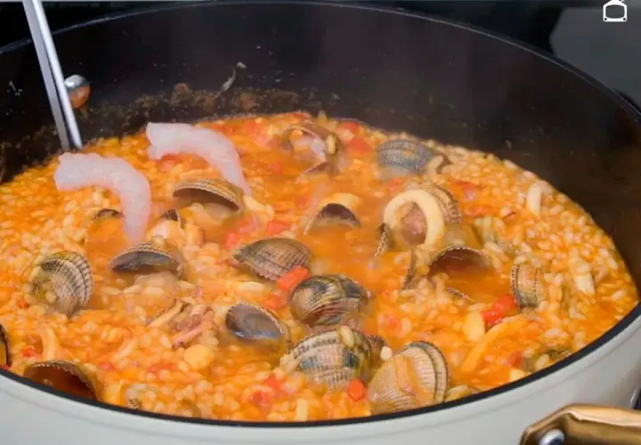 Un delicioso arroz a la marinera burbujea en una sartén, con gambas, almejas y calamares.