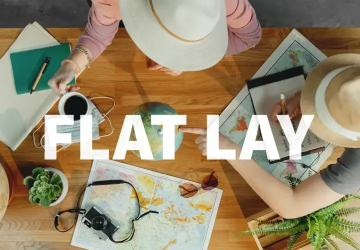 Widok z góry na stół z mapami, globusem, aparatem i notatkami. Dwie osoby planują podróż, tworząc inspirujący **flat lay**.