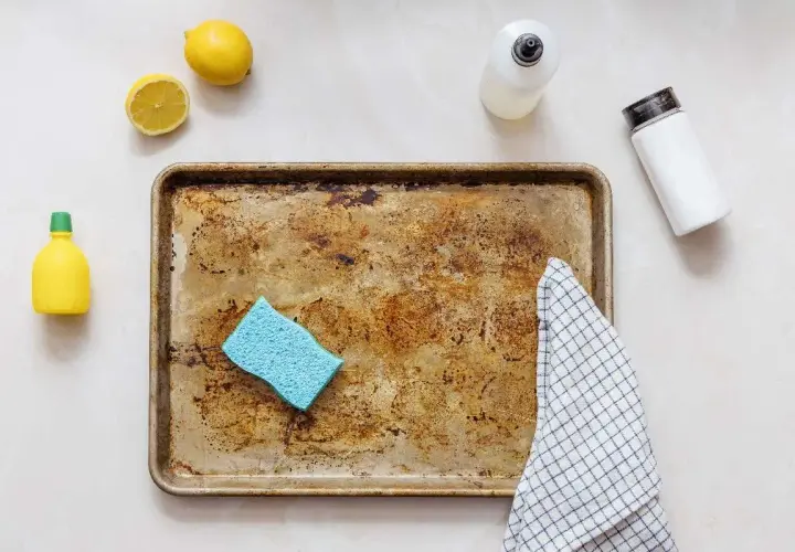 Une plaque de cuisson en aluminium très sale, une éponge bleue, des citrons, une bouteille de produit vaisselle et une serviette à carreaux, prêts à décaper l'aluminium.
