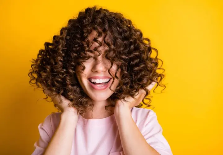Mujer sonríe con cabello rizado y voluminoso. Descubre cómo hidratar el cabello después de una permanente para mantenerlo así de saludable.