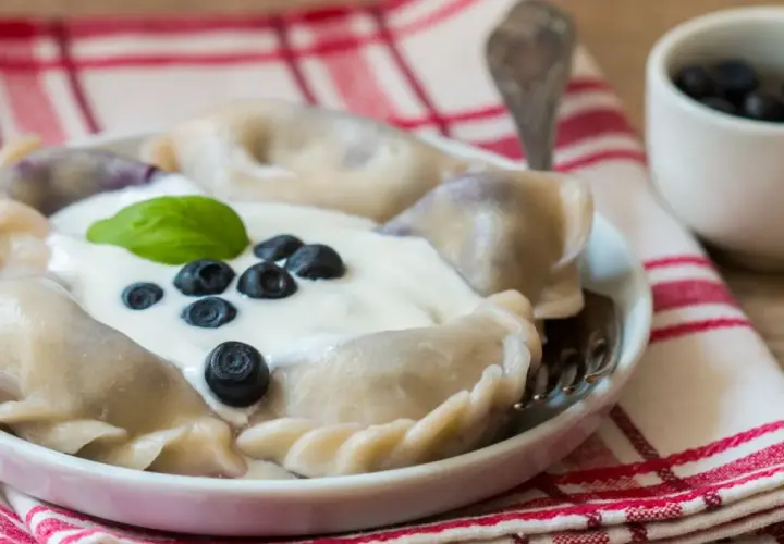 Pyszne pierogi z borówkami amerykańskimi, polane śmietaną i ozdobione świeżymi owocami. Idealne na letni deser.